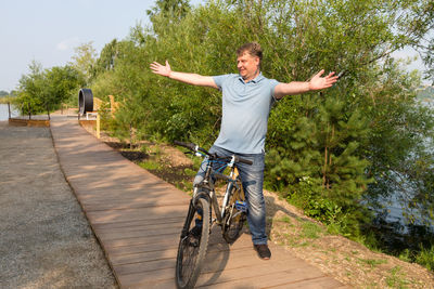 An adult smiling man bicycle calls a friend with a hand gesture.