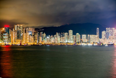 Illuminated cityscape by sea against sky at night