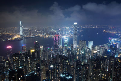 Illuminated cityscape at victoria harbour against sky