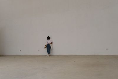 Full length of woman standing against white wall on floor