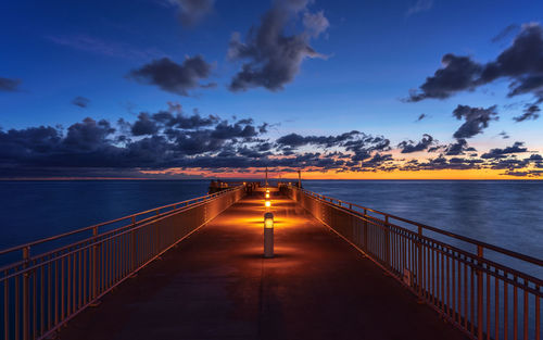 Illuminated bridge over sea against sky during sunset