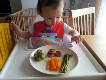 Close-up of baby girl eating food while sitting on high chair at home