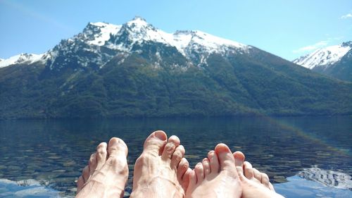 Low section of bare feet against calm lake