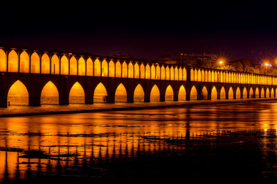 Illuminated bridge over river against sky at night