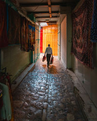 Rear view of woman walking in alley amidst buildings