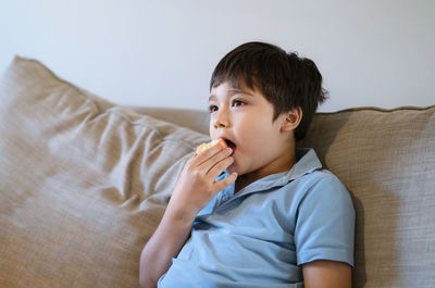 Boy eating apple while sitting on sofa at home