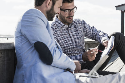 Two businessmen with notepad and tablet working outdoors