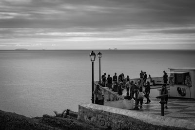 People on hill by sea against cloudy sky