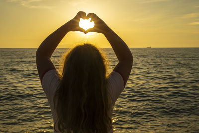 Rear view of woman standing by sea against sky during sunset