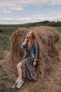 Full length of woman sitting by hay stack