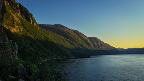 Scenic view of river by mountains against clear sky