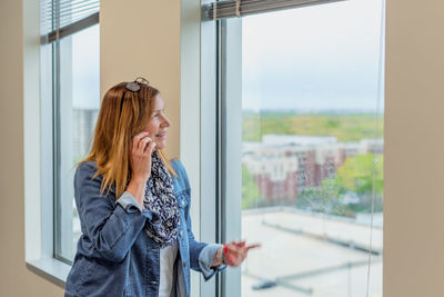 Woman looking away while standing against window