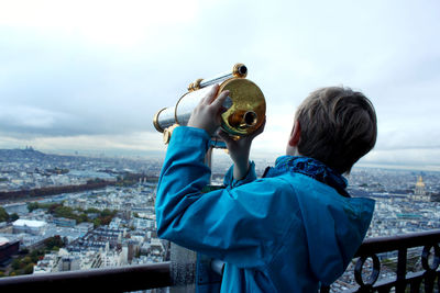 Rear view of teenage boy holding coin-operated binoculars at observation point in city