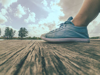 Low section of person on wooden floor against sky