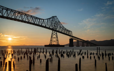 Silhouette bridge over sea against sky during sunset