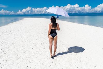 Rear view of bikini woman standing with umbrella on beach against sea