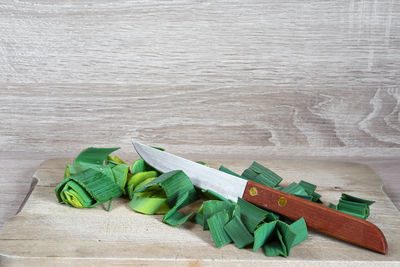 Close-up of leek and knife on cutting board at wooden table