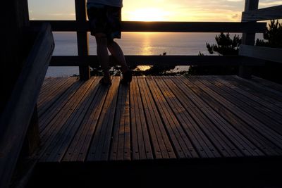 Low section of silhouette man standing on sea at sunset