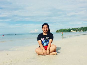 Portrait of smiling young woman sitting on shore at beach