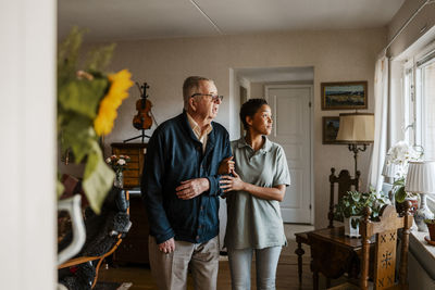 Female caretaker standing arm in arm with senior man at home