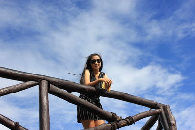 Low angle portrait of woman sitting on railing against sky