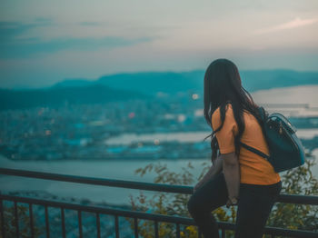 Woman sitting on railing against city