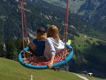 High angle view of siblings swinging on mountain against forest