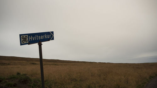 Road sign on field against sky
