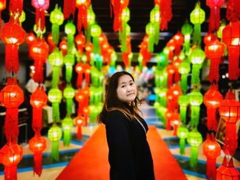 Portrait of woman standing amidst illuminated lanterns