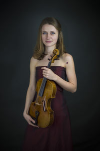 Portrait of young woman standing against black background