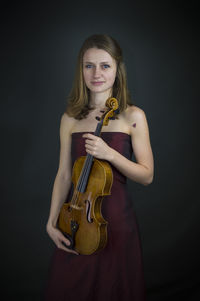 Portrait of woman holding violin against black background