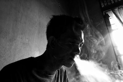 Close-up of man emitting smoke against wall at home