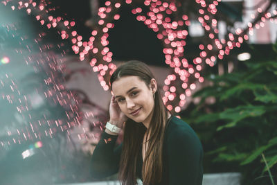 Portrait of smiling young woman against illuminated lights and plants