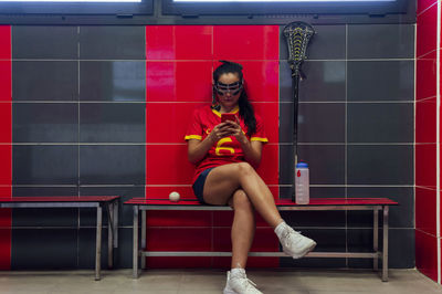 Player using smart phone sitting in lacrosse locker room