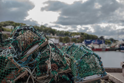 Close-up of fishing net at harbor against cloudy sky