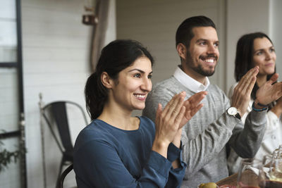 Smiling business professionals clapping while sitting at table during winetasting