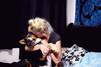 Woman embracing pembroke welsh corgi while sitting on bed