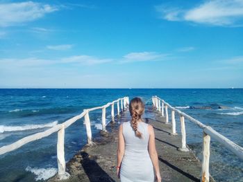 Rear view of woman standing on pier against sky