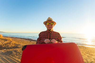 Man sitting on beach by sea against sky