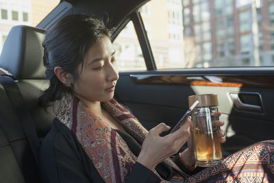 Young asian businesswoman looking at smartphone sitting in car service limousine