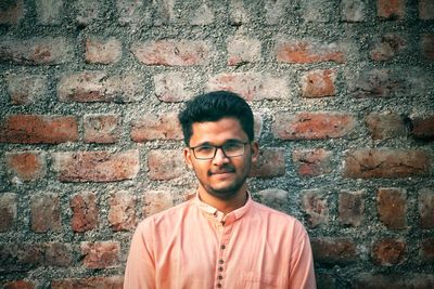 Portrait of smiling young man standing against brick wall