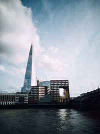 View of building by river against cloudy sky