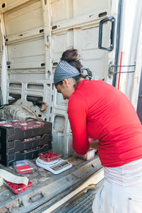 Side view of attentive female gardener measuring weight of ripe raspberries on digital scales in van trunk