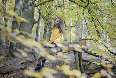 Portrait of girl sitting on tree trunk in forest