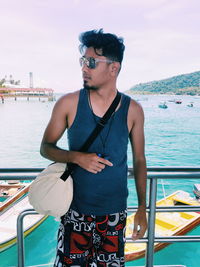 Young man wearing sunglasses standing by sea against sky
