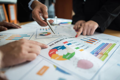 Midsection of business people working over graphs on table at office