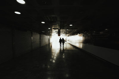 Rear view of silhouette man walking in illuminated tunnel