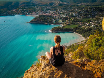 Rear view of woman sitting on rock by sea