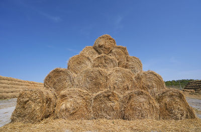 Hay bales on field against blue sky