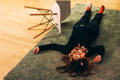 High angle view of mid adult woman with illuminated string lights lying on carpet at home